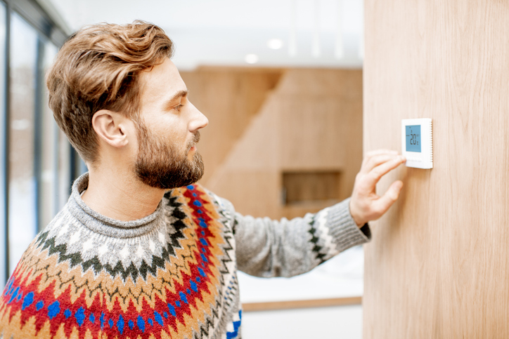 Man in wollen stripey jumper setting the temperature at a wall thermostat