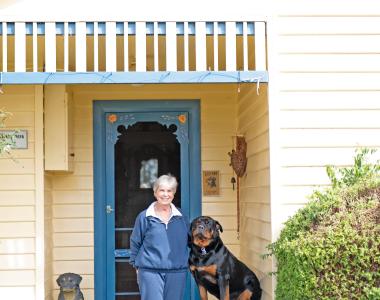 A woman and her dog outside a weatherboard house.